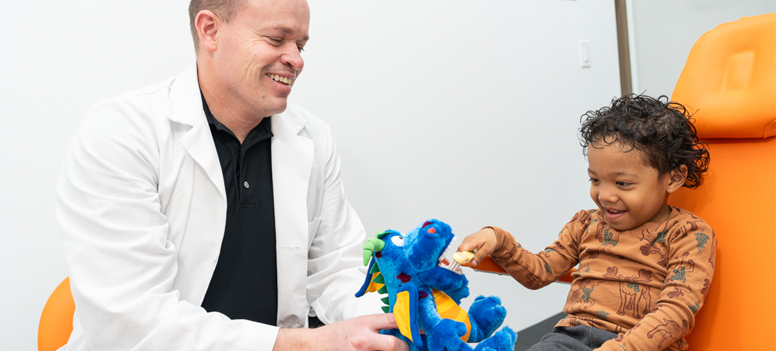 Dr. Mason showing a boy how to brush his teeth using stuffed animals as an example