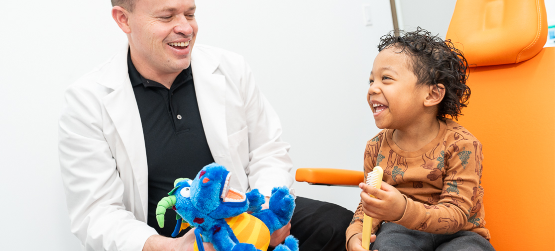 Dr. Mason showing a boy how to brush his teeth using stuffed animals as an example